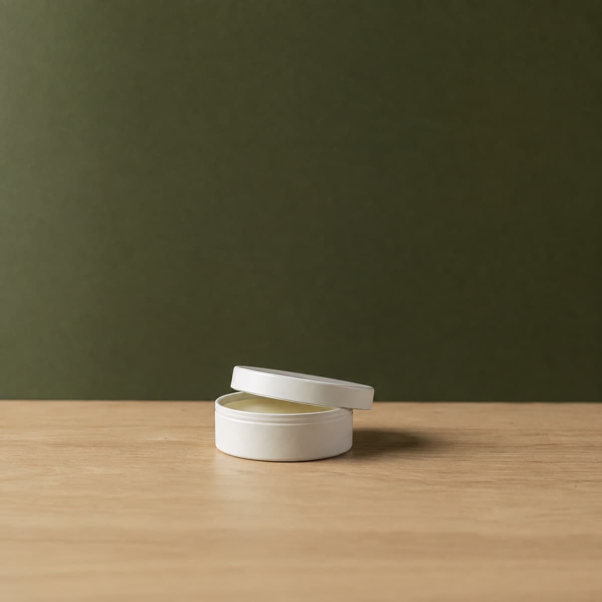Care Balm Travel Tin 50 ml — wax-white packaging on an oak surface against a moss-green background