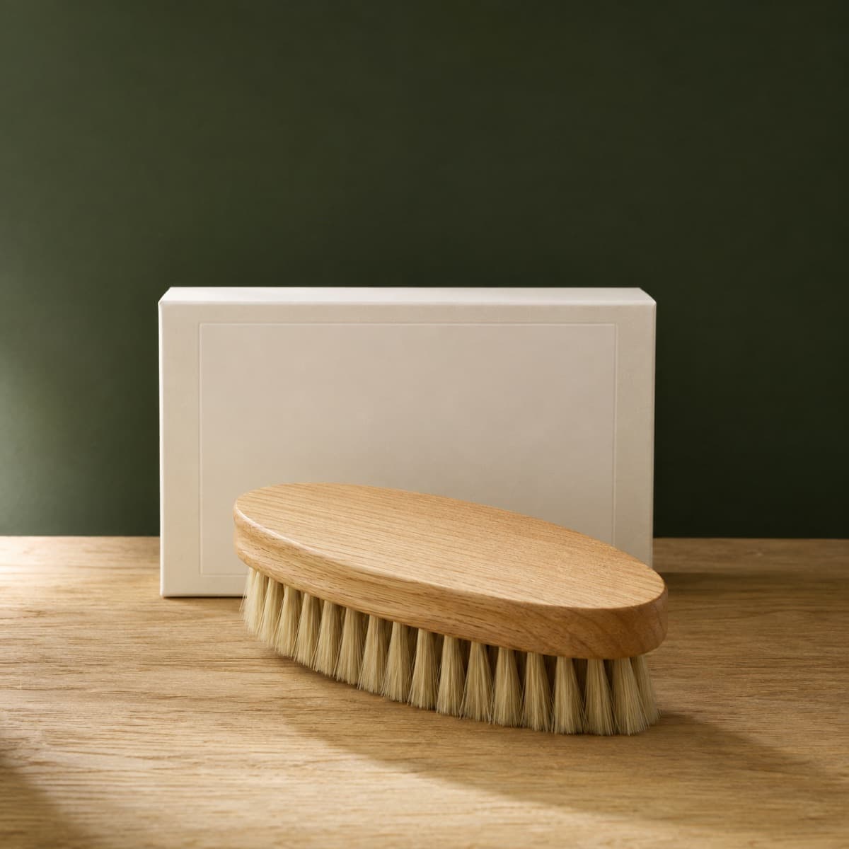 Horsehair Brush Large — wax-white packaging on an oak surface against a moss-green background